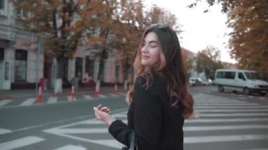 Şık siyah elbiseli zarif bir genç kız yaya geçidinde karşıdan karşıya geçer ve muhteşem saçlarını düzeltir.