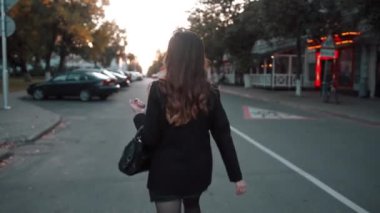 Şık giyinmiş genç bir iş kızı bir kafenin neon ışıklarını geçerek yola çıkıyor ve kameraya dalgalı saçlarıyla dönüyor.