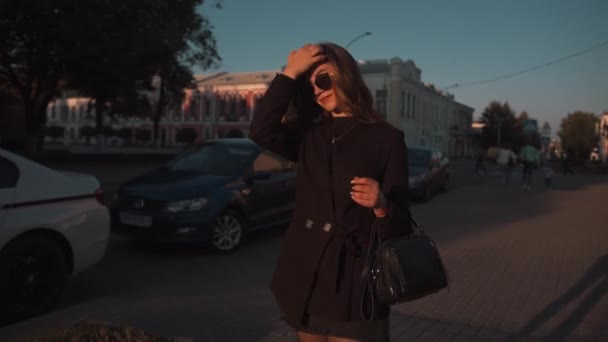 Krásná mladá dívka v černých šatech a slunečních brýlích prochází historickou čtvrtí města a při západu slunce si užívá procházku. Zpomalený pohyb — Stock video