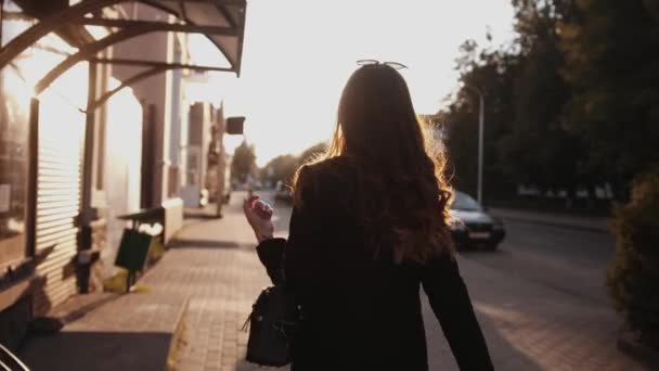 Чуттєва молода дівчина з довгим волоссям в стильному одязі йде по міській вулиці і обертається з мерехтливим волоссям на заході сонця. Повільний рух — стокове відео