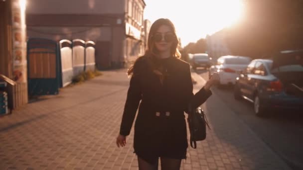 Spektakularna młoda dziewczyna w okularach przeciwsłonecznych idzie wzdłuż ulicy miasta i zwraca się do kamery prostowania jej wspaniałe włosy. Zwolniony ruch — Wideo stockowe