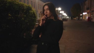 Güzel bir genç kız akşam bir şehir caddesinde elektronik sigara içiyor ve bir duman bulutu salıyor. Yavaş çekim