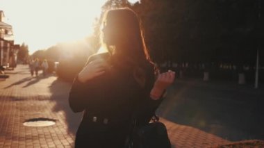 Sofistike bir genç bayan güneş gözlüğü takar ve gün batımında şehir sokaklarında dikilirken lüks saçlarını düzeltir.