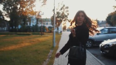 Şık siyah elbiseli, başında güneş gözlüğü olan muhteşem bir genç kız gün batımında şehir sokaklarında dolaşır.