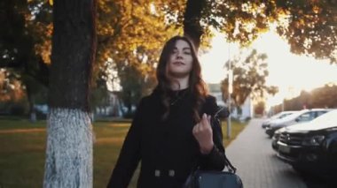 Uzun, lüks saçları olan şık bir genç kız elinde bir çantayla şehir caddesinde dolaşıyor ve gülümsüyor. Yavaş çekim