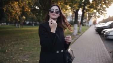 Şık siyah elbiseli, başında güneş gözlüğü olan muhteşem bir genç kız gün batımında şehir sokaklarında dolaşır.