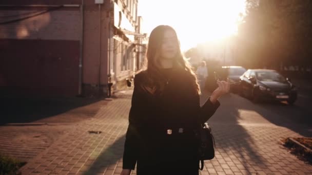 Krásná mladá dívka ve stylových černých šatech prochází městem při západu slunce a nasazuje si sluneční brýle na hlavu. Zpomalený pohyb — Stock video