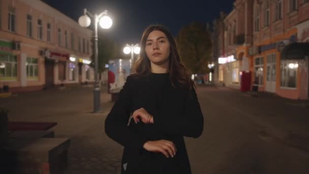 A flirtatious young girl goes along the evening street with her arms crossed over her chest and straightens her gorgeous hair — Stock Video