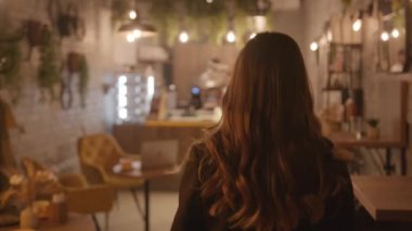 Güzel genç bir kız, canlı bitkilerle süslenmiş bir kafenin koridorunda yürüyor ve elinde dizüstü bilgisayarla bir masaya oturuyor.