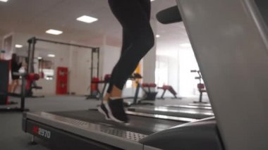 Bobruisk, Belarus - 9 Eylül 2021: Spor salonunda koşu bandı üzerinde kardiyo çalışması yapan enerjik genç kadın kalça ve kalça kaslarını güçlendirir