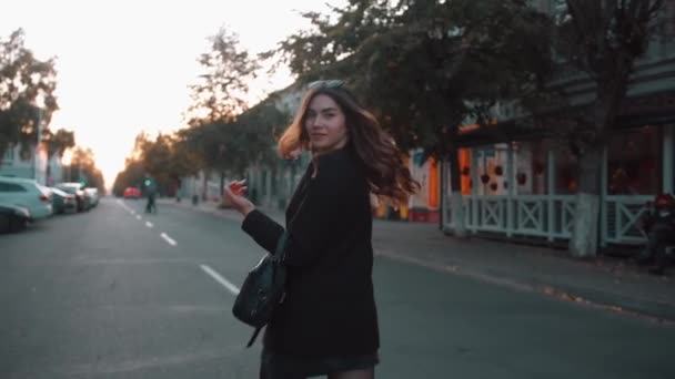 Obchodní mladá dívka ve stylovém oblečení jde na silnici kolem neonových světel kavárny a otáčí se s chvějícími se vlasy na kameru — Stock video
