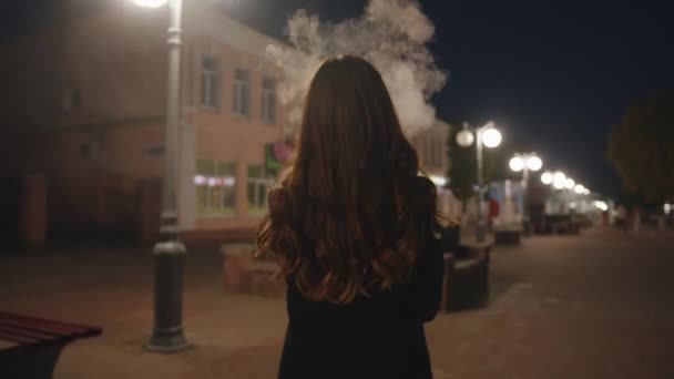 Een schattig jong meisje in stijlvolle zwarte kleren gaat langs de avondstraat en geniet van het uitzicht op de stad. Langzame beweging — Stockvideo
