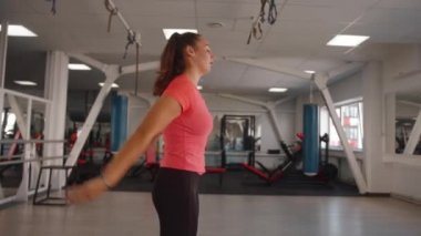 Terli tişörtlü genç bir kadın spor salonunda antrenman yaptıktan sonra esneyerek Delta ve Rotator omuz kelepçelerini geriyor.