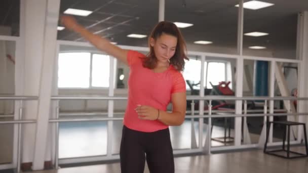 Красивая молодая девушка в розовой футболке разогревается перед тренировкой и делает круговые движения руками — стоковое видео
