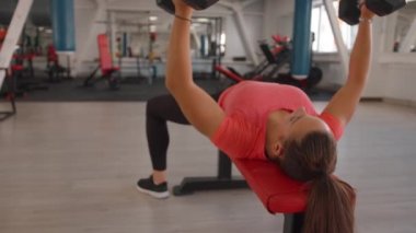 Kafasında at kuyruğu olan genç bir kadın spor kulübünde çalışıyor ve elleri için egzersiz yapıyor.
