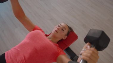 Pembe tişörtlü ve taytlı genç bir kadın bir spor kulübünde ve spor yapıyor.