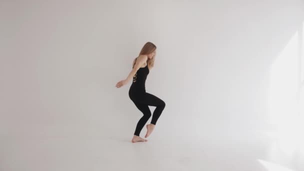 Красива молода дівчина займається розтягуванням з елементами класичного танцю і граціозно рухається в білій студії — стокове відео