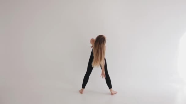 Гибкая юная девушка босиком занимается растяжкой с элементами классического танца в студии на белом фоне — стоковое видео