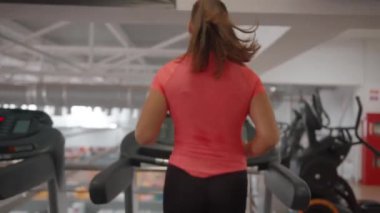 Spor salonundaki koşu bandında siyah spor ayakkabılı ve siyah taytlı kadın bacakları. Arkadan bak. Yavaş çekim