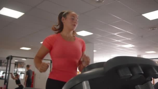 Mujer joven enfocada haciendo entrenamiento cardiovascular en el gimnasio y corriendo en la cinta de correr para quemar calorías y fortalecer los músculos. Movimiento lento — Vídeos de Stock