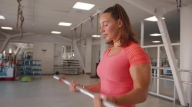 Güzel bir genç kız spor salonunda antrenman yapıyor ve ayakta halter kaldırıyor. Yavaş çekim