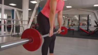 Spor salonundaki genç bir kız meyilli halter sırasına girer ve latissimus dorsi ve trapezius kaslarını sallar.