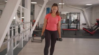 Güzel bir genç kız spor salonunun etrafında dolanıyor ve elinde dambıllarla hamleler yapıyor. Yavaş çekim
