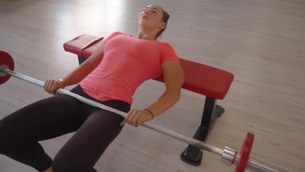 Νεαρό κορίτσι στο γυμναστήριο εκτελεί μια πυελική ανελκυστήρα σε ένα πάγκο barbell να αντλήσει τους μυς του πίσω μέρος του μηρού και κοιλιακούς μυς — Αρχείο Βίντεο