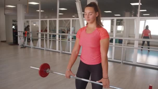 Una chica joven realiza una fila de pesas con una inclinación en el gimnasio para bombear los músculos trapecio y la parte posterior de los deltoides — Vídeo de stock