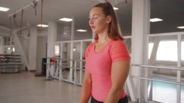 Hoş bir genç kız kollarını kaldırıyor spor salonunda dambıllar ile trapezius kası ve deltoidi pompalamak için. Yavaş çekim