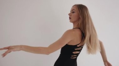 Şehvetli genç kız stüdyoda dans öğeleriyle meşgul ve kolları ve vücuduyla yumuşak hareketler yapıyor.