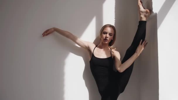 Souriant jeune fille faisant étirement et de mettre sa jambe sur le mur et debout dans une fente verticale appuyé sur le mur — Video