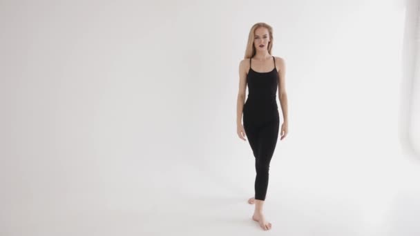 Энергичная молодая девушка в обтягивающей черной одежде делает качели ноги и принимает вертикальный раскол. Концепция гармонии и баланса — стоковое видео