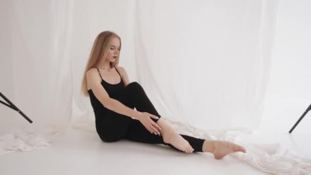 Uma jovem sensual está fazendo alongamento no estúdio contra o fundo de pedaços de tule branco. Movimento lento — Vídeo de Stock