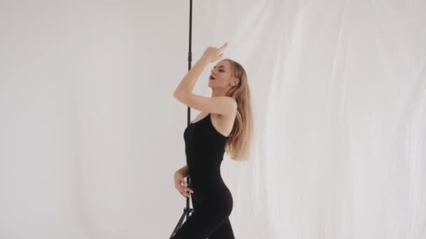 Egy gyönyörű fiatal lány fekete szűk ruhában és mezítláb nyújtózkodik a stúdióban, és simán mozog, mint egy táncban. Lassú mozgás. — Stock videók