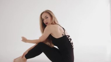 Siyah bluzlu, parlak makyajlı ve taytlı genç bir kız yerde oturmuş elleriyle dizlerini birbirine yapıştırıyor. Yavaş çekim