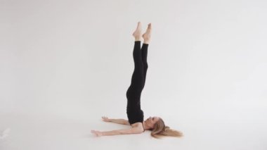 Çekici bir genç kız yerde yatarak huş ağacı egzersizi yapıyor ve bacaklarını başının üstüne atıyor. Yavaş çekim