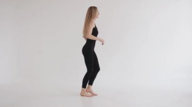 Güzel bir genç kız stüdyoda esneme hareketleri yapıyor ve bale tutumundaki gibi bacağını kaldırıyor. Yavaş çekim