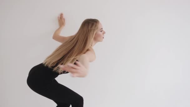 Zmysłowa młoda dziewczyna rozciąga się w białym studio i porusza się płynnie wykorzystując elementy tańca klasycznego. Zwolniony ruch — Wideo stockowe