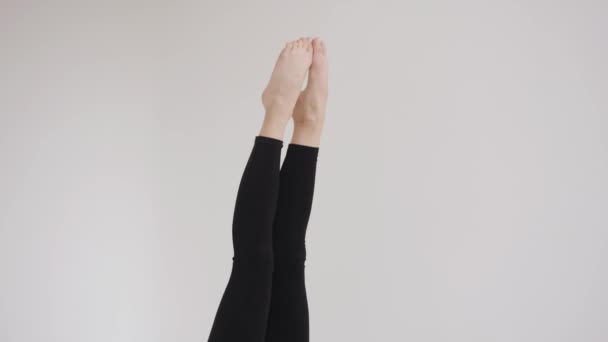 Ein schlankes junges Mädchen in schwarzem Top und Leggings macht eine Birkenübung und wirft sich in Stretchkursen die Beine über den Kopf. Zeitlupe — Stockvideo