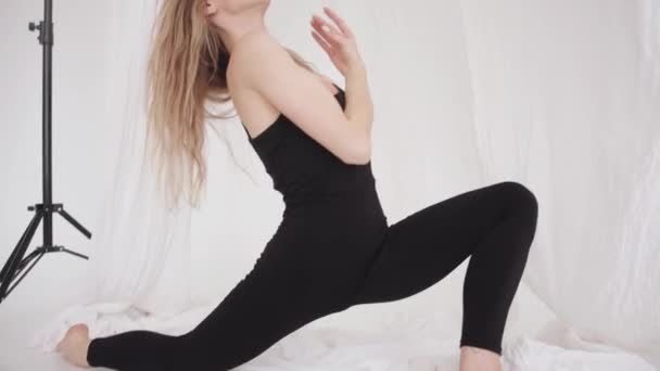 En vacker ung flicka är engagerad i stretching i studion och gör en djup lunge med mjuka rörelser av hennes armar. Långsamma rörelser — Stockvideo