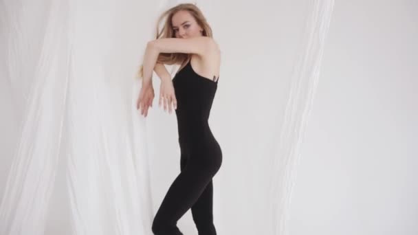 En sensuell ung flicka i svart åtsittande overall rör sig vackert i en klassisk dans bland den flödande vita tyllen. Långsamma rörelser — Stockvideo