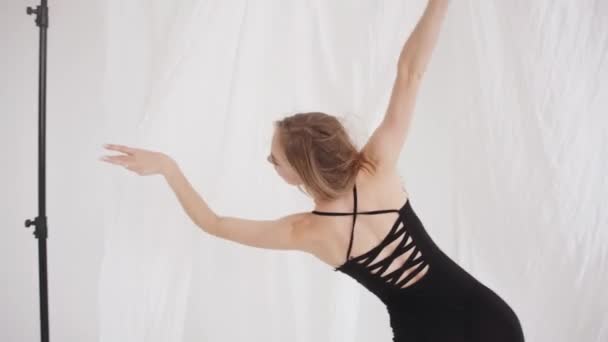 Espectacular jovencita se estira en el estudio y utiliza elementos de danza clásica entre piezas colgantes de tul blanco. Movimiento lento — Vídeos de Stock
