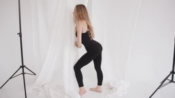 A sensual young girl in a black tight-fitting jumpsuit moves beautifully in a classical dance among the flowing white tulle. Slow motion — Stock Video