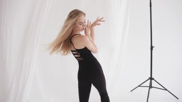 Захватывающая молодая девушка растянута в студии и использует элементы классического танца среди висячих кусочков белого тюля. Медленное движение — стоковое видео
