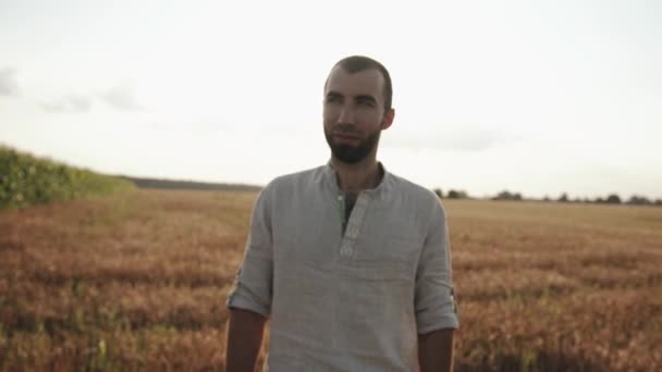 Mladý muž s vousy v bílé košili projde pšeničným polem. Koncept samoty a reflexe. Zpomalený pohyb — Stock video