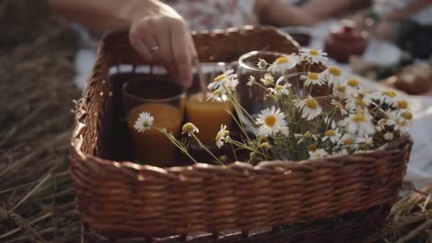 Máma dává sklenici džusu se slámou do košíku s kyticí sedmikrásek během rodinného pikniku v přírodě. Detailní záběr. Zpomalený pohyb — Stock video