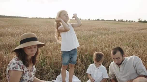 Une charmante fille montre le mouvement de ses mains dans une danse et chante lors d'un pique-nique avec ses parents et son frère cadet. Mouvement lent — Video