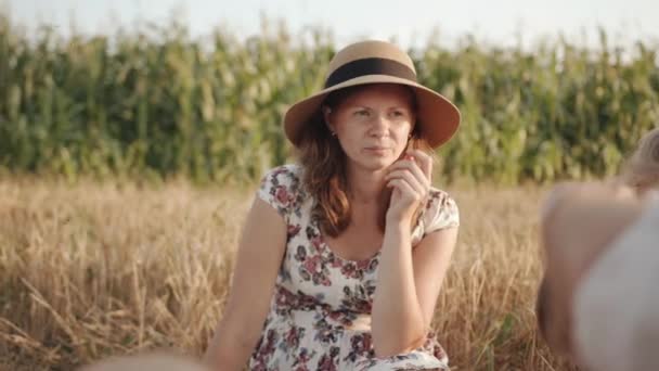 Bir yaz elbisesi içinde dingin bir anne ve hasır bir şapka, çocuklarını buğday tarlasında aile kazmasında yer ve seyreder. Yavaş çekim — Stok video