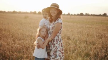 Küçük çocuklarıyla birlikte mutlu bir anne buğday tarlasında duruyor ve küçük oğlu şapkasına dokunuyor. Yavaş çekim